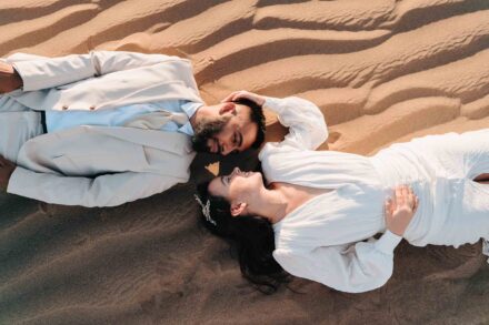 Los novios, tumbados en la arena cabeza con cabeza y en sentidos opuestos, sonríen con las caras juntas, desde arriba