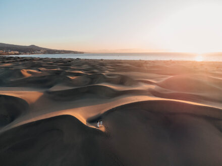 Los novios, diminutos entre las dunas de Maspalomas (Gran Canaria), con el sol bajo sobre el mar