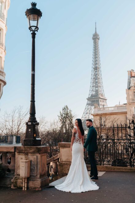La novia mira atrás por encima del hombro, de la mano del novio, junto a una farola frente a la torre Eiffel