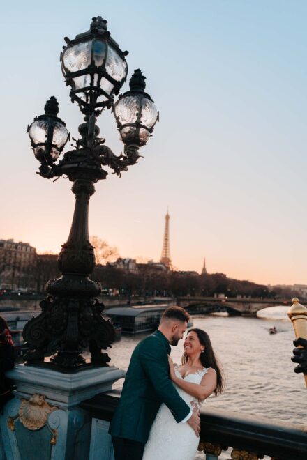 Los novios se abrazan junto a una gran farola de un puente sobre el río, con la torre Eiffel al fondo