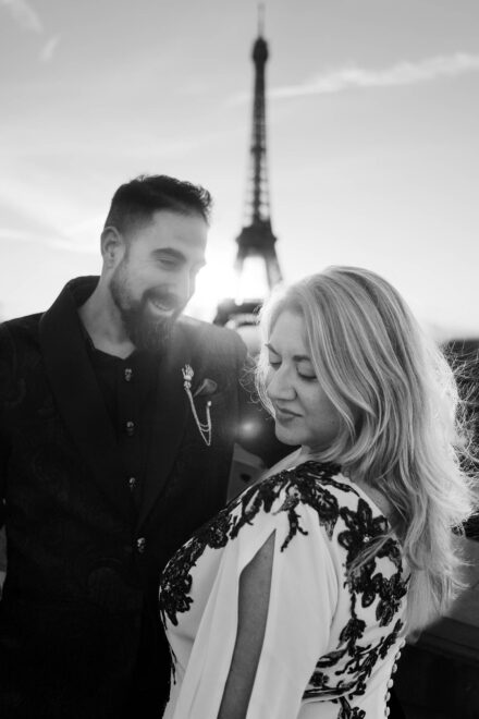 La novia sonríe con la mirada baja y el novio se ríe a su lado, a contraluz ante la torre Eiffel