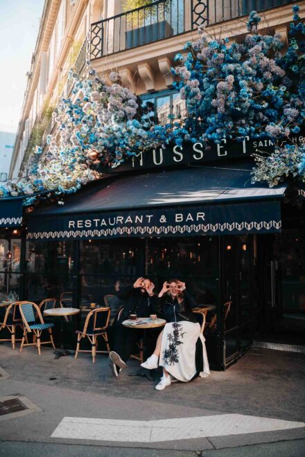 Los novios se ponen macarons delante de los ojos en la terraza de un café con flores azules en la fachada