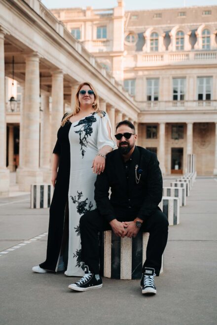 Los novios, con gafas de sol, posan: ella de pie y él sentado en una columna a rayas blancas y negras