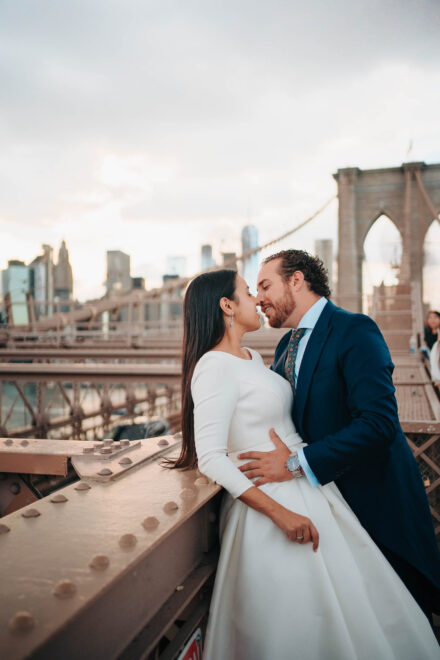 Los novios se rozan la nariz apoyados en la barandilla del puente de Brooklyn, con los rascacielos detrás