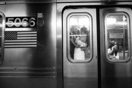 Los novios se abrazan tras la ventanilla de un vagón de metro, junto a una bandera de Estados Unidos