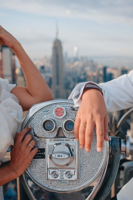 Las manos de los novios con sus alianzas sobre unos prismáticos de monedas, con el Empire State detrás
