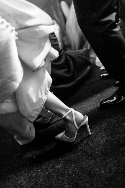 La novia se recoge el vestido en la pista y deja ver su zapato de tacón con tira al tobillo, en blanco y negro