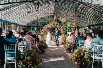 Ceremonia en un antiguo invernadero de hierro y cristal, con los novios bajo un arco de flores