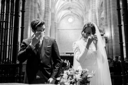 Los novios se secan las lágrimas con pañuelos ante el altar de una iglesia gótica, en blanco y negro