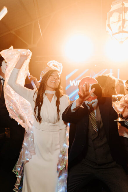 La novia agita un tul de luces con los ojos cerrados junto a un invitado con gorro de flamenco rosa