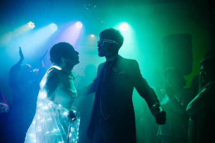 La novia, envuelta en un tul con luces, baila frente al novio con gafas luminosas bajo focos verdes y azules
