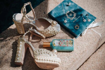 Sandalias de plataforma con perlas y un perfume junto a una libreta de terciopelo azul con anillos y pendientes