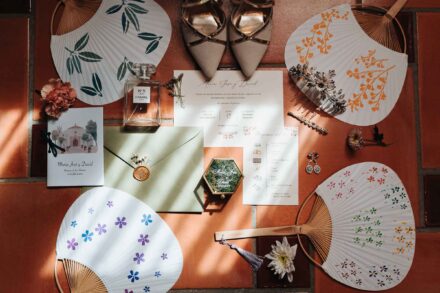 Abanicos pintados, invitación, zapatos, perfume y pendientes de la novia sobre un suelo de barro