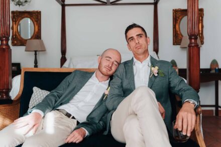 Dos invitados con americana verde en un sofá; uno apoya la cabeza en el hombro del otro con los ojos cerrados