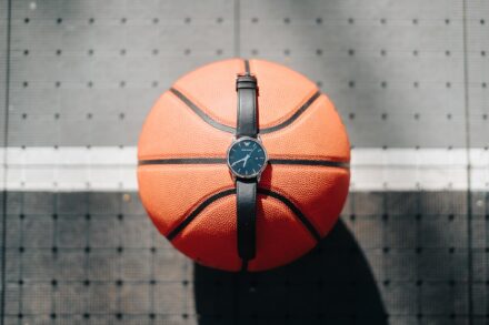 Un reloj de correa negra apoyado sobre un balón de baloncesto en el suelo de la pista