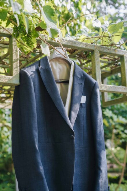 La chaqueta azul del novio cuelga de una pérgola cubierta de parra