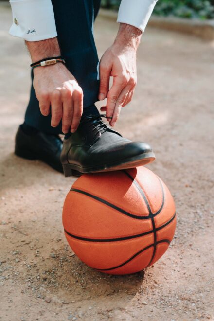 El novio se ata el zapato negro con el pie apoyado sobre un balón de baloncesto