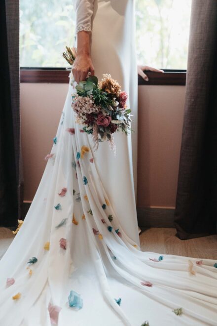 La larga cola del vestido de la novia, salpicada de pétalos de colores, y el ramo junto a la ventana