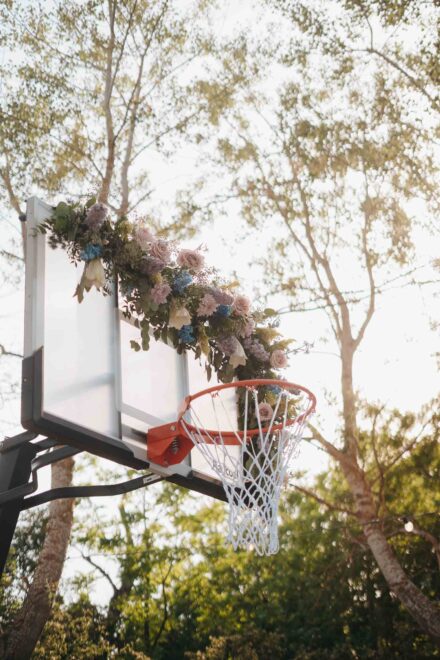 La canasta de baloncesto decorada con flores rosas y azules, vista desde abajo entre los árboles
