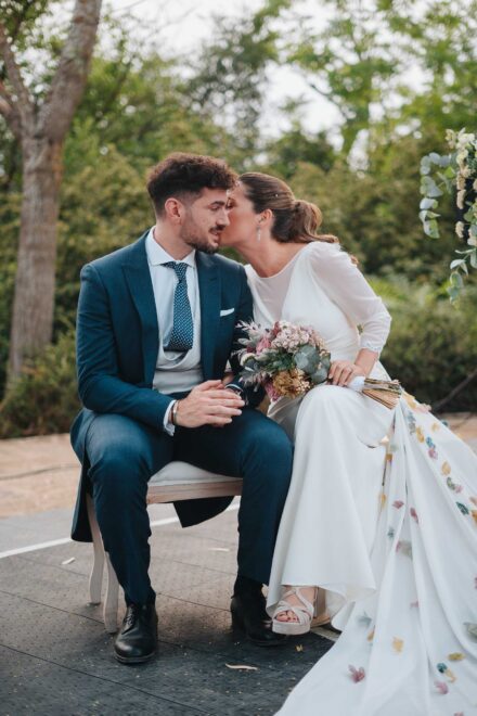 La novia besa al novio en la mejilla, sentados en el banco durante la ceremonia