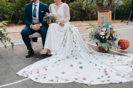 Los novios sentados en la pista, con la cola salpicada de pétalos de colores extendida junto a un balón y flores