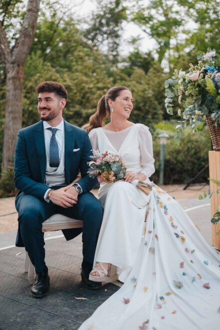 Los novios se ríen sentados en el banco de la ceremonia, mirando los dos hacia un lado