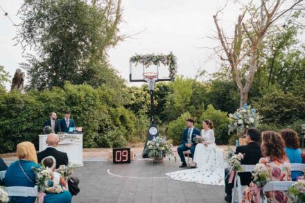 Ceremonia en la pista de baloncesto: los novios bajo la canasta y los invitados sentados, en el Balneario El Raposo