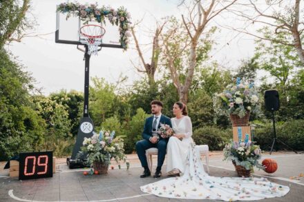 Los novios sentados en el centro de la pista, bajo la canasta con flores y junto al marcador en «09»