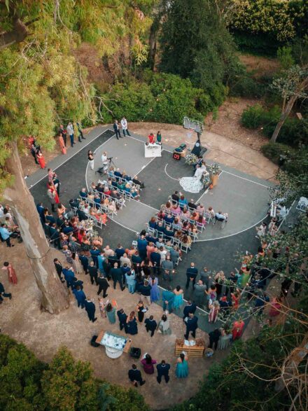 Vista aérea de la ceremonia en la pista de baloncesto rodeada de árboles e invitados, en el Balneario El Raposo