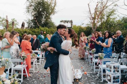Los novios se besan en el pasillo de la ceremonia entre los invitados, bajo una lluvia de pétalos