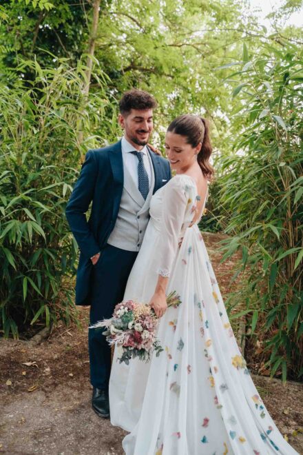 Los novios posan abrazados entre cañas de bambú, ella sonriente con el ramo en la mano