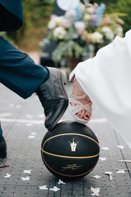 El zapato del novio y la sandalia de la novia pisan a la vez un balón de baloncesto negro y dorado