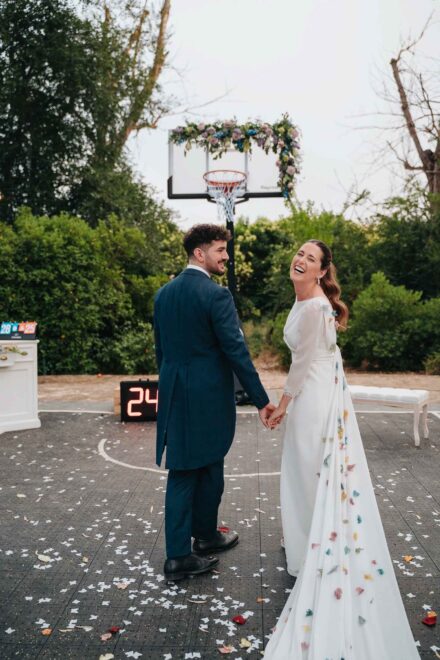 Los novios de la mano sobre la pista cubierta de pétalos, ella riendo a carcajadas bajo la canasta