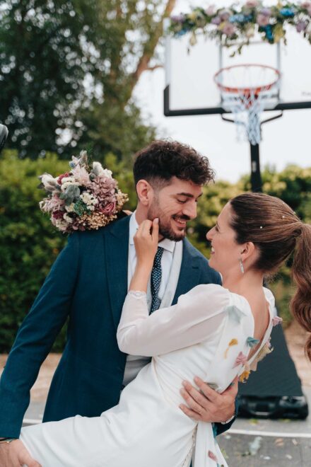 La novia acaricia la barba del novio mientras él la sujeta por la cintura, junto a la canasta