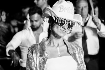 Una mujer con sombrero vaquero con «Bride» en brillantes, gafas de corazón y chaqueta de lentejuelas, en blanco y negro